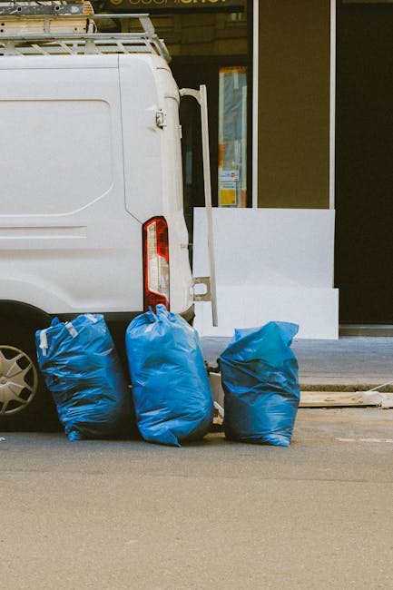 A large accumulation of black plastic rubbish bags stacked against a modern building with a tiled exterior in an urban environment. The bags are tightly sealed, some appear slightly bulging, and a few