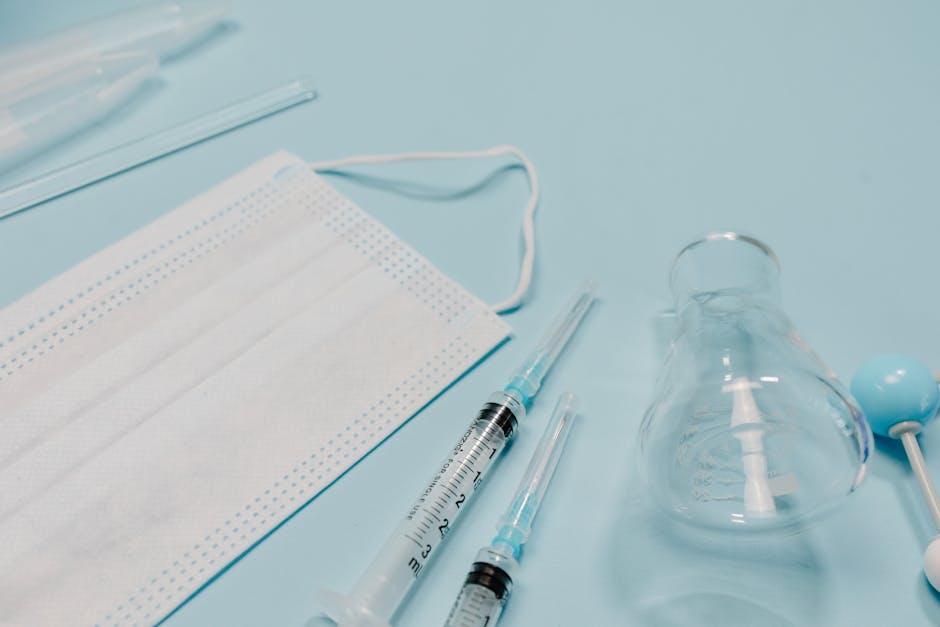 A collection of five disposable syringes with clear plastic barrels and black rubber plungers, situated on a textured white paper surface. The syringes vary in size, with visible measurement markings